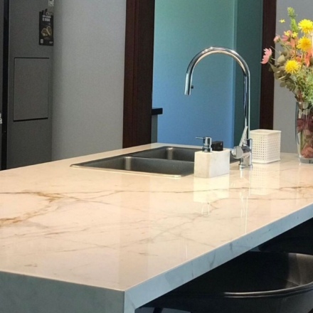 Foto de una mesada de cocina de cuarzo blanco simil mármol carrara. La cocina es moderna, tiene una bacha plateada y un jarrón con flores encima de la mesada.