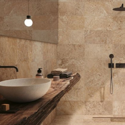 Foto de un baño integramente hecho en travertino. El baño parece un spa, muy moderno. Con iluminación suave, duchador y bacha de madera.
