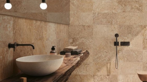 Foto de un baño integramente hecho en travertino. El baño parece un spa, muy moderno. Con iluminación suave, duchador y bacha de madera.